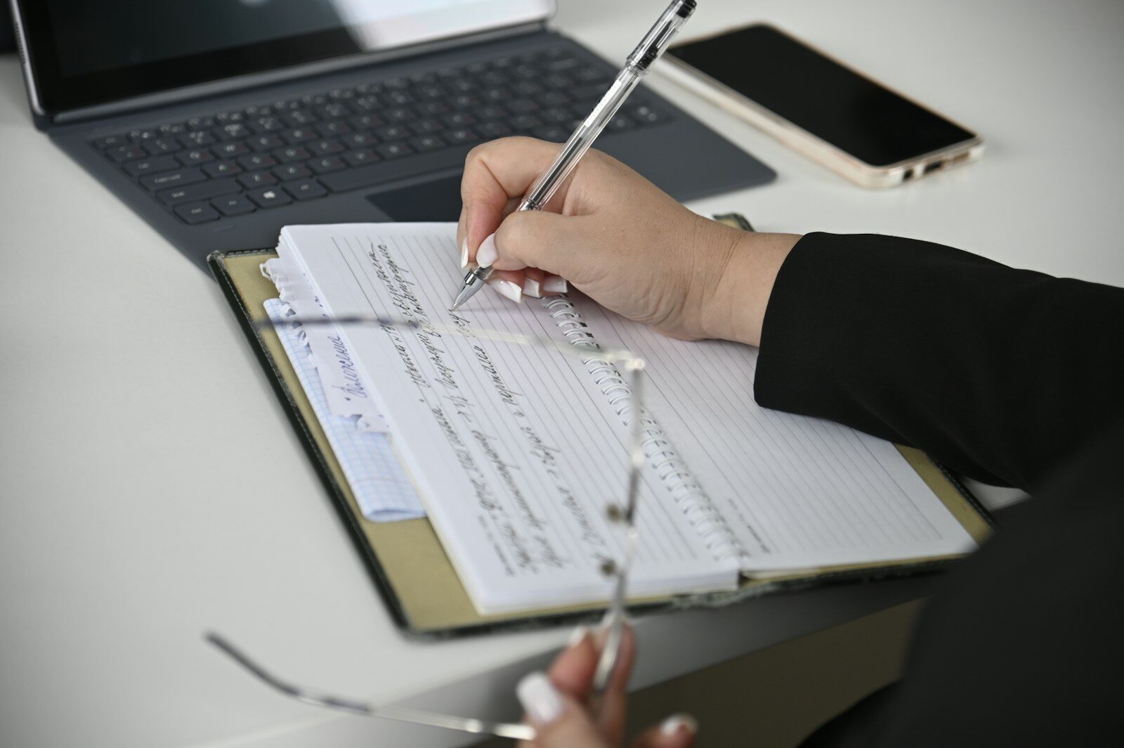 Un personne écrivant sur un papier avec un ordinateur en fond. Photo de