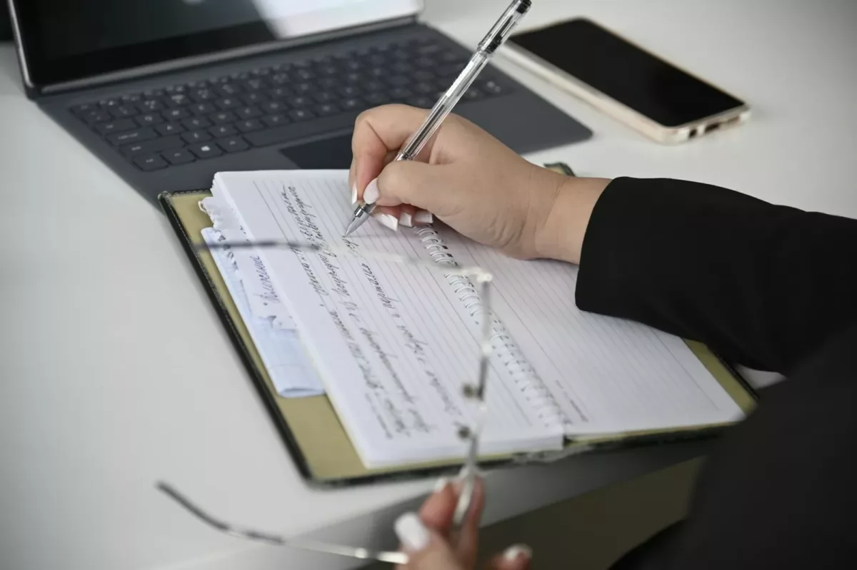 Un personne écrivant sur un papier avec un ordinateur en fond. Photo de